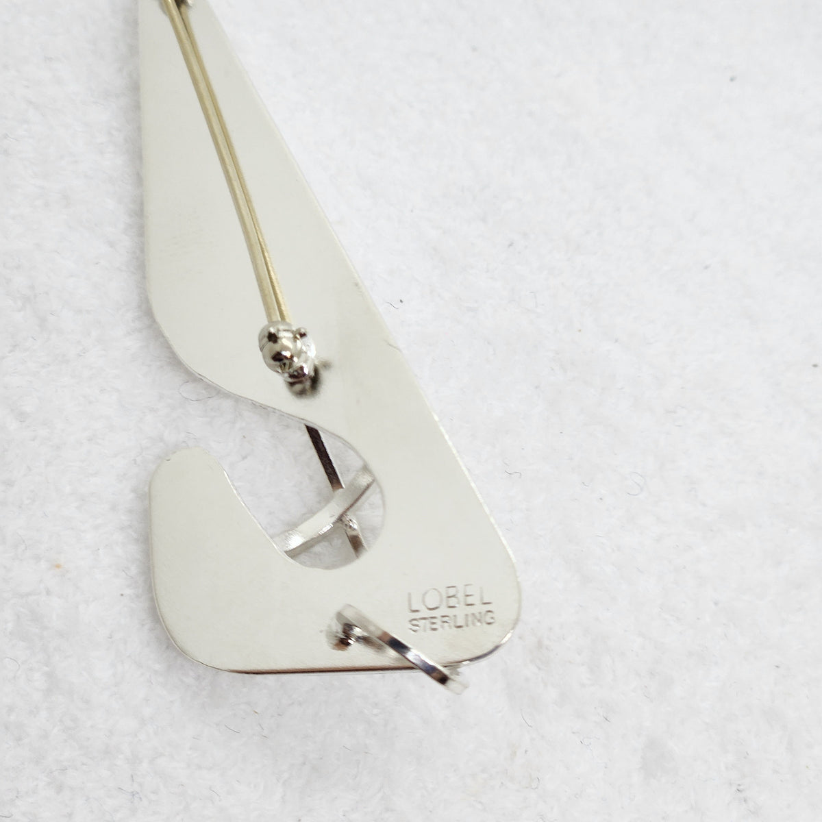 A sterling silver brooch with a polished, reflective finish, featuring the engraved brand name 'LOBEL STERLING' on one of its prongs. The pin is displayed on a textured white background.