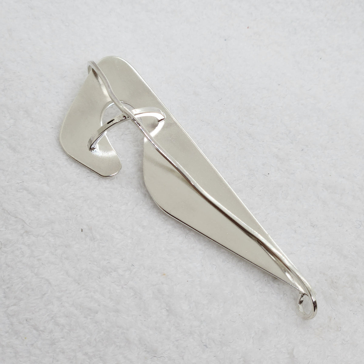 A polished silver pendant with an abstract, organic leaf-like shape and a central loop, displayed on a textured white background.