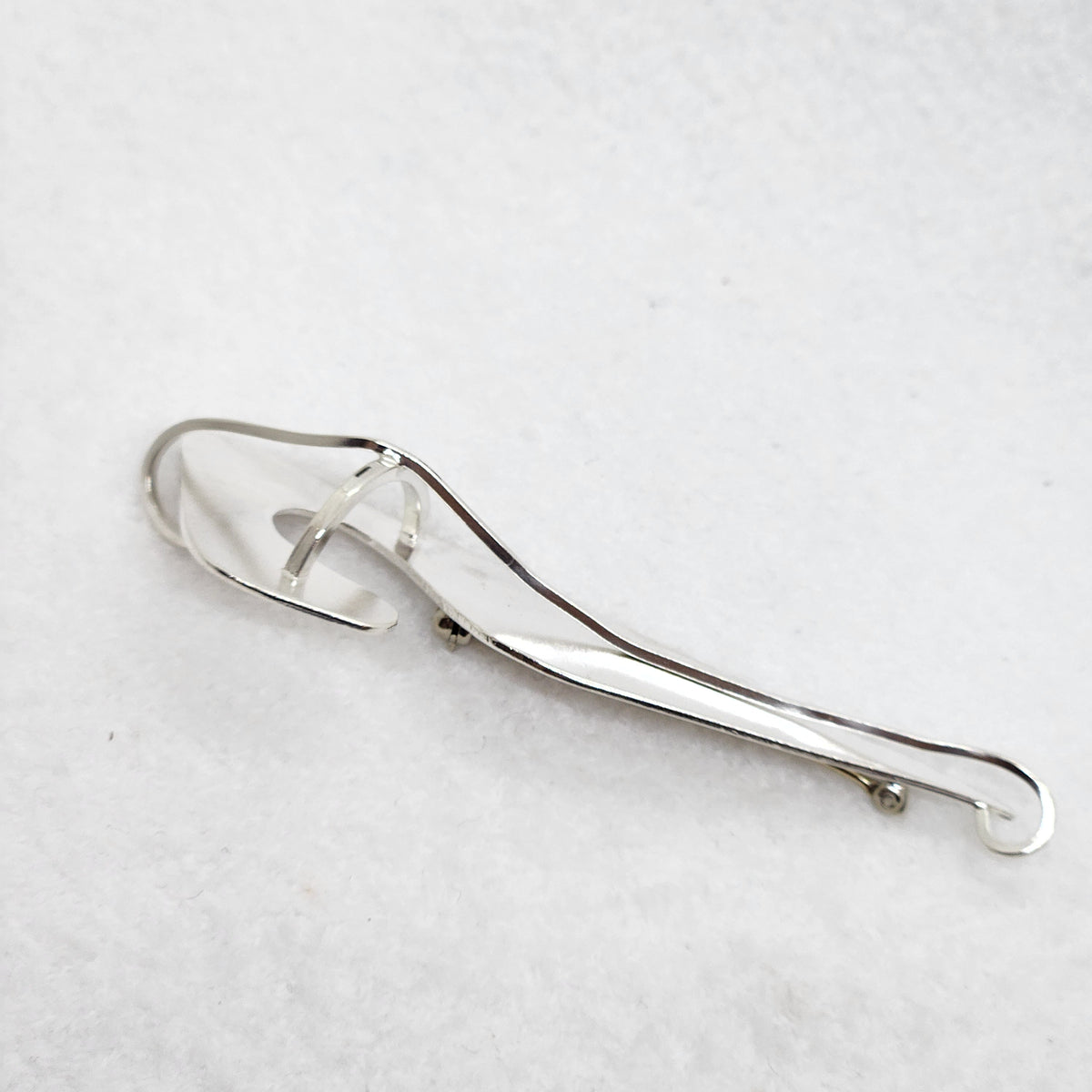 A polished silver pendant with an abstract, organic leaf-like shape and a central loop, displayed on a textured white background.