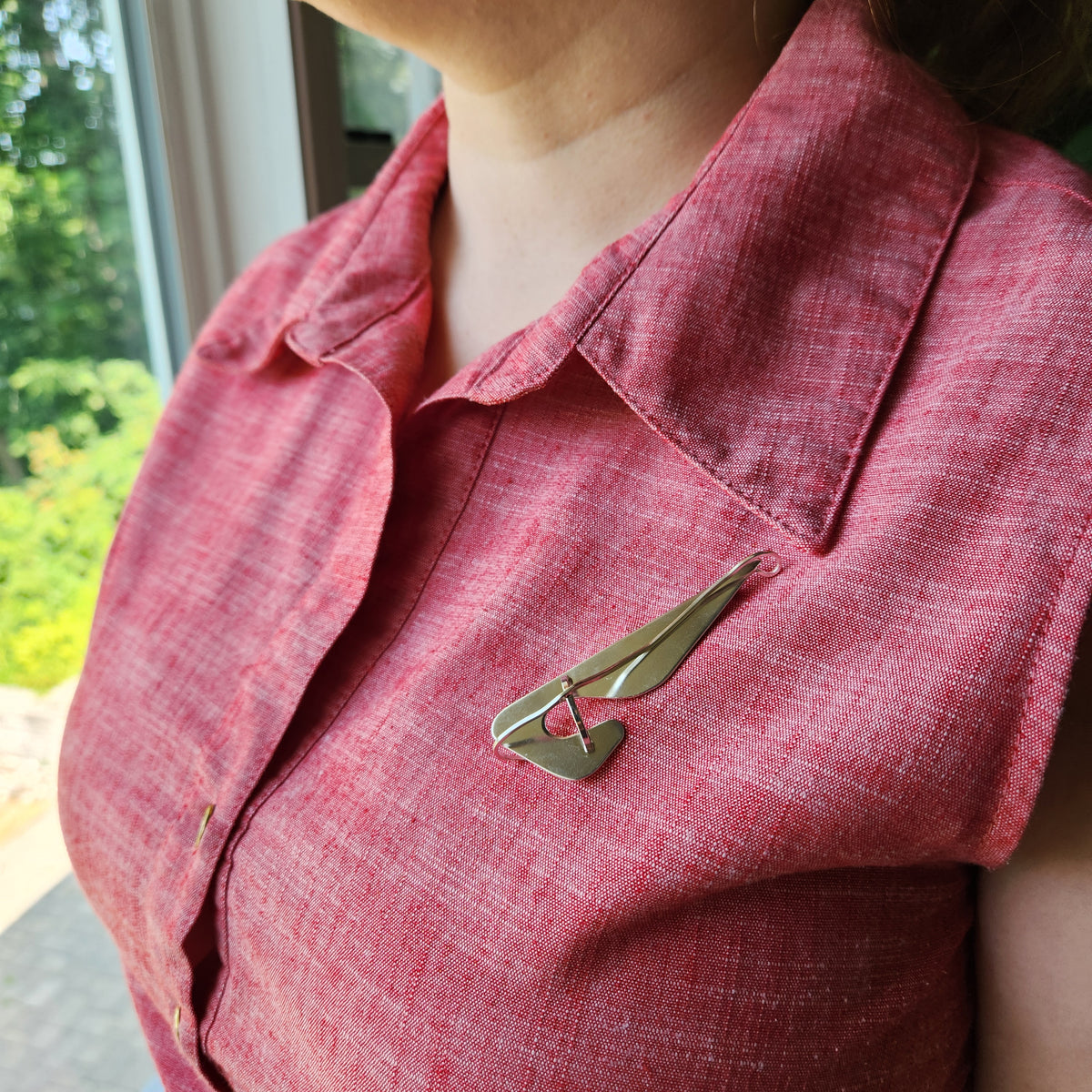 A close-up of a person wearing a textured red linen shirt and a silver wing-shaped brooch pinned to the chest.