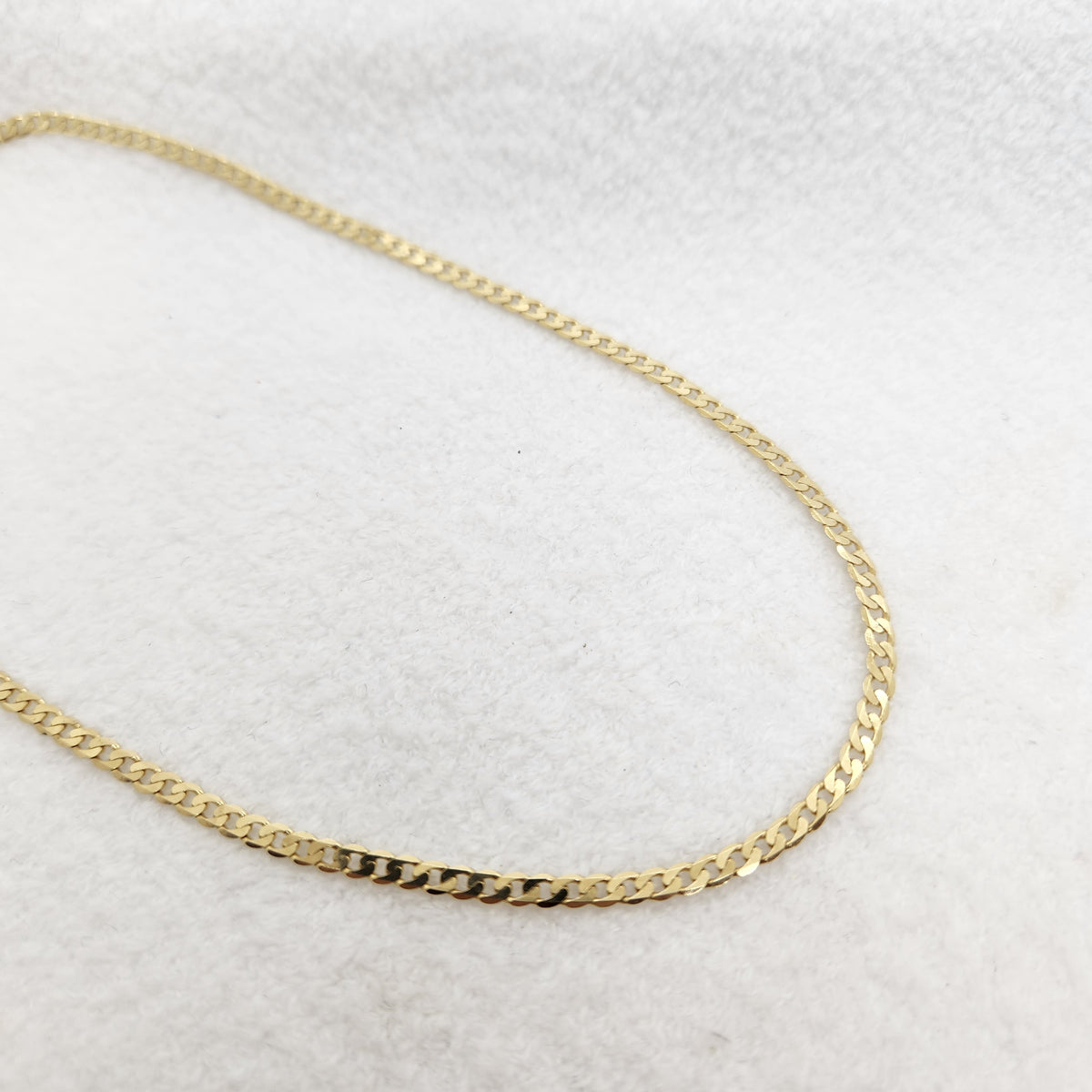 A gold-toned Cuban link chain necklace displayed on a textured white fabric background.